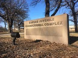 Kansas Juvenile Correctional Complex sign beside a mailbox in a leaf-covered outdoor setting