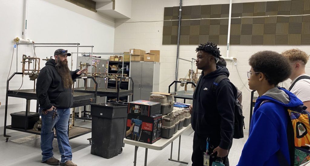 People standing in a workshop near tables with tools and equipment, one person using a camera.