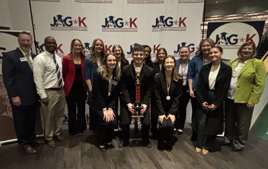 Group of people posing in front of a MAG-K backdrop at a formal event, dressed in business attire.