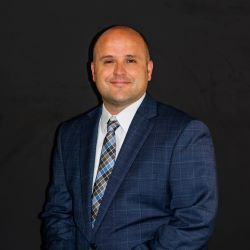Man in a blue plaid suit and tie posing against a dark background