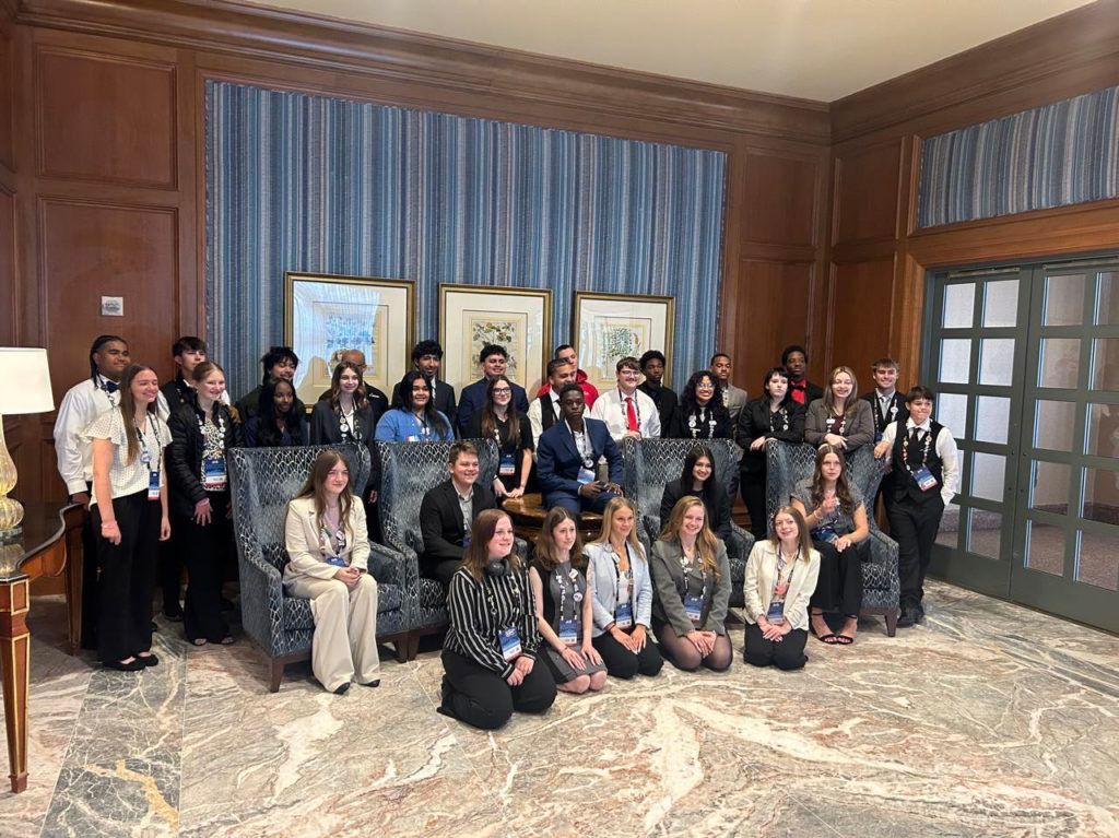 Group posing in a wood-paneled room with a marble floor, framed art, and a large window.
