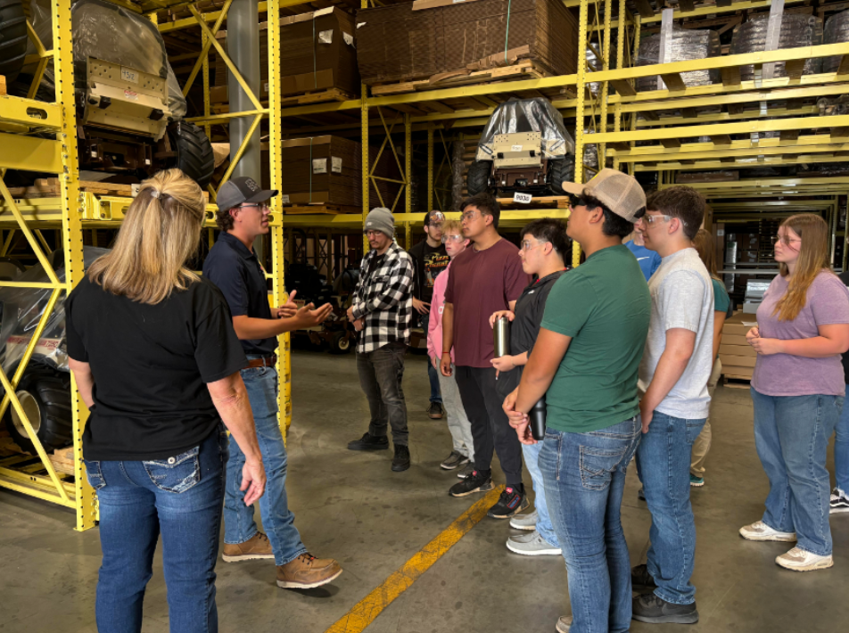 Group of people listening to a guide in an industrial warehouse with yellow racks and large machinery.