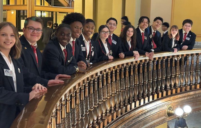 Group of students in uniforms leaning on an ornate balcony inside a grand building