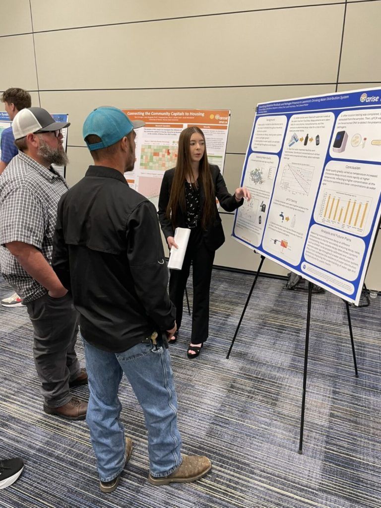 Presenter explaining research poster to three attendees at conference display boards