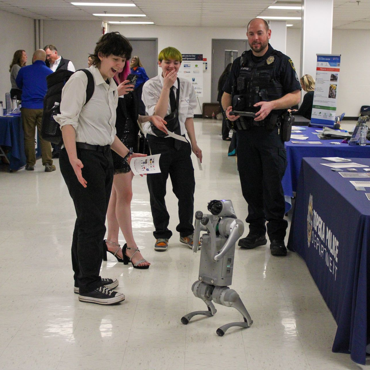 People watching a small humanoid robot demonstration at an indoor event booth