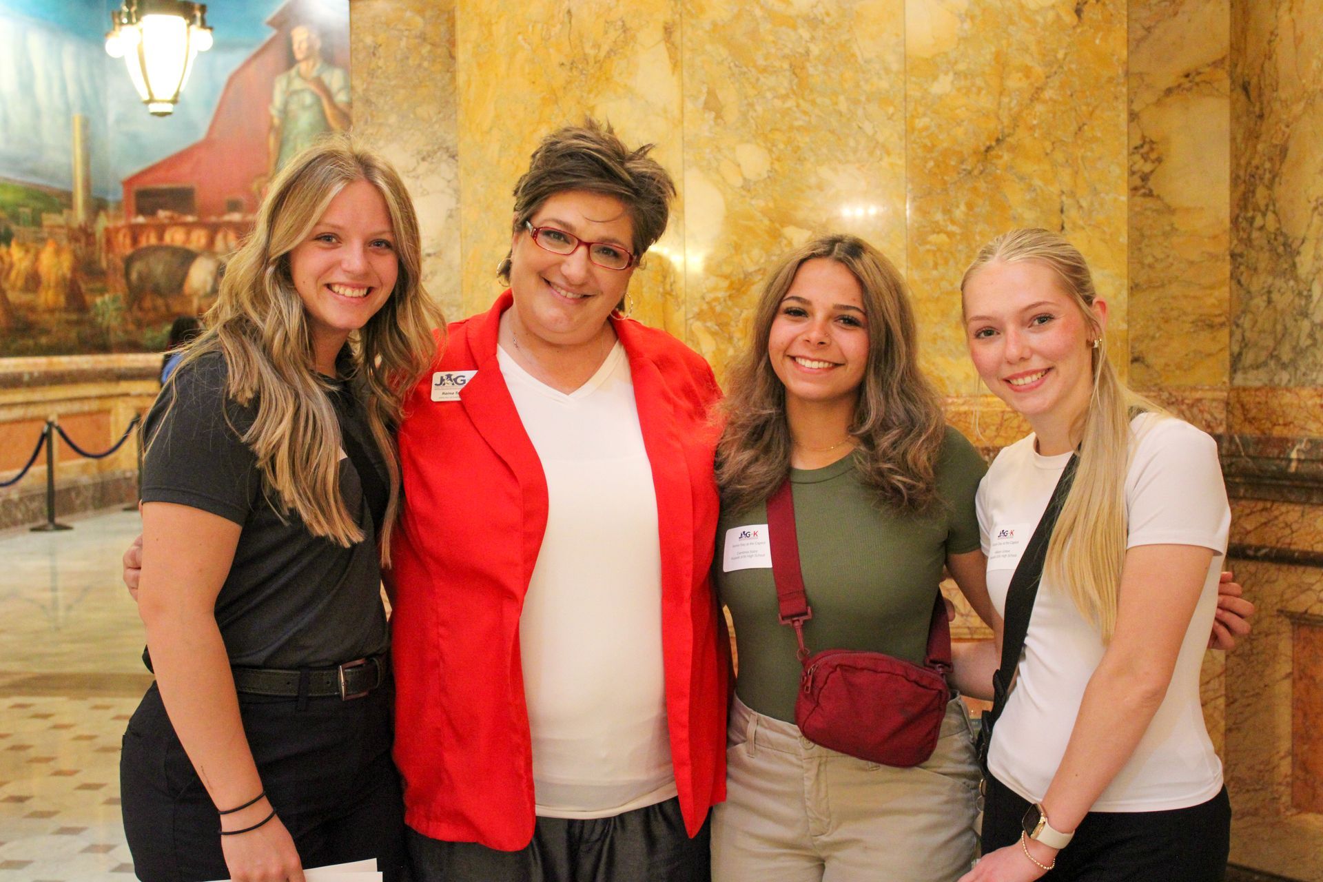 Four people smiling in a marble hallway, with one wearing a red jacket.