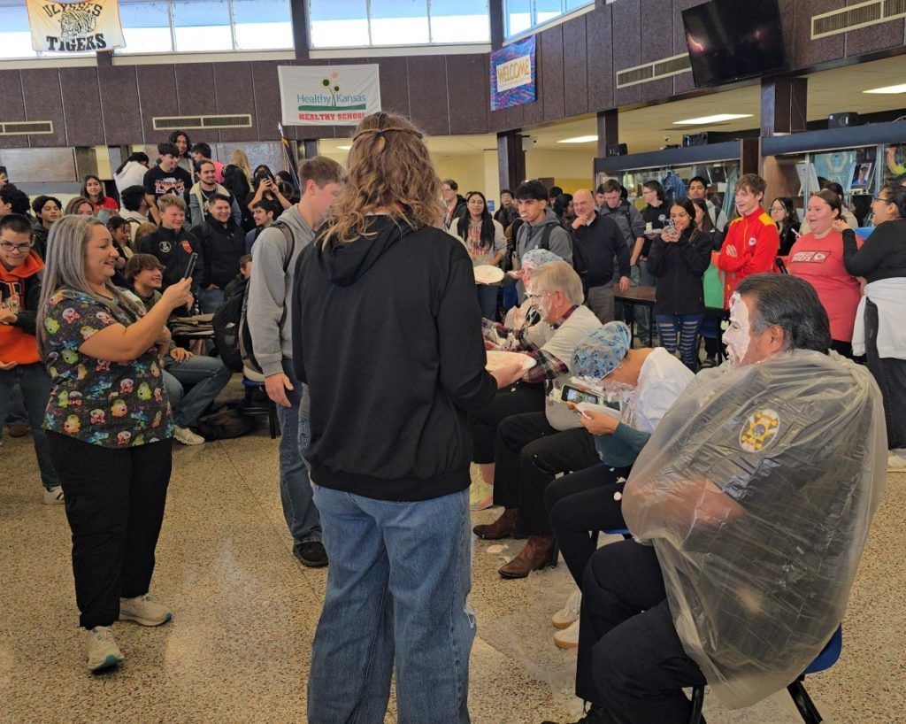 Crowded indoor gathering with people applauding and speaking in a busy public hall