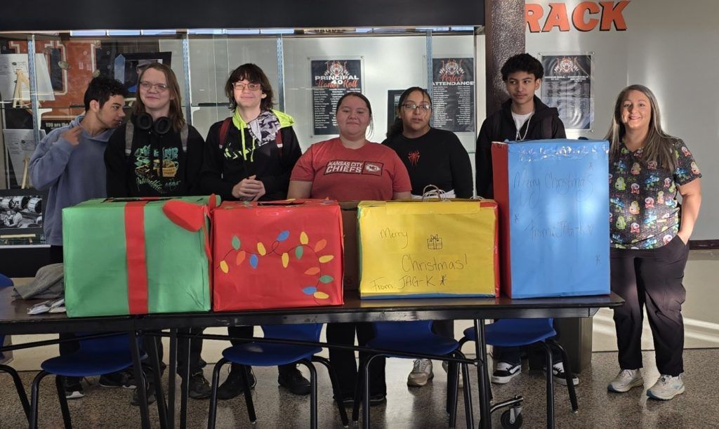 Six people stand behind colorful display boards at a table in a classroom or event space.