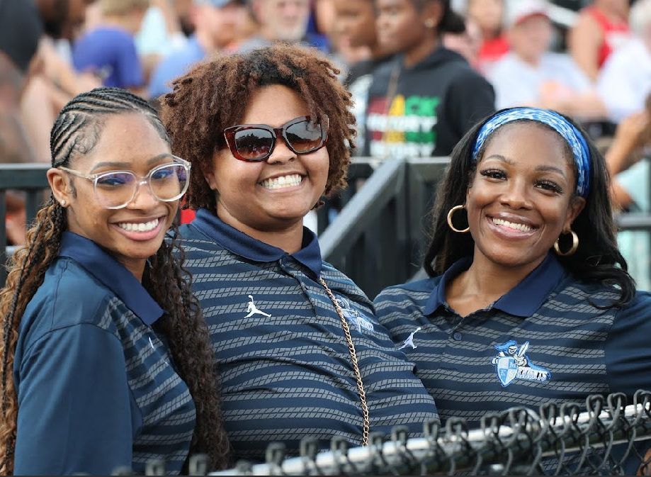 Three smiling fans in navy striped shirts posing at a sports event