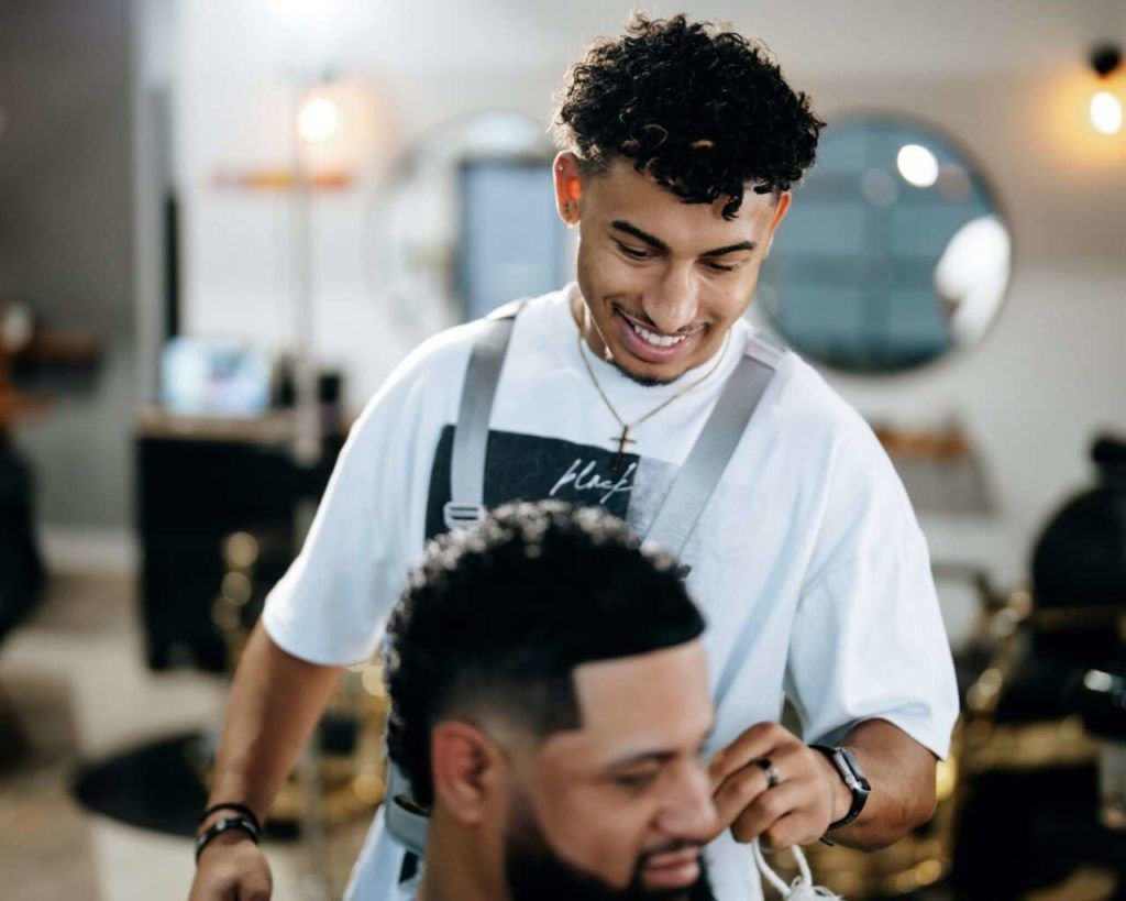 Barber smiling while cutting a client's hair in a bright barbershop