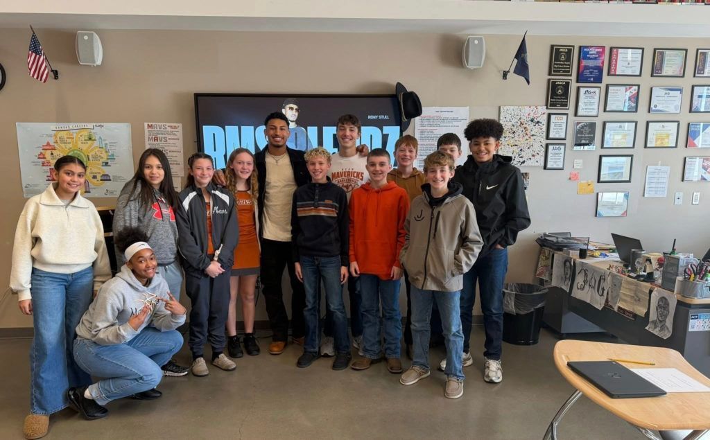 Group of people posing in a classroom with a TV screen and wall displays behind them