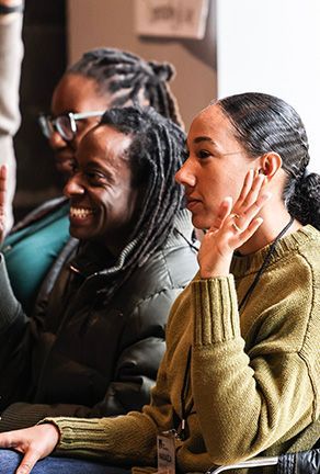 Three people seated indoors, listening attentively, one in a green sweater with her hand near her face.