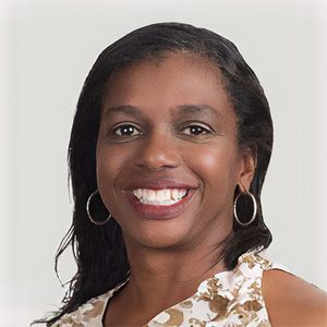 Smiling woman in a white floral top with hoop earrings against a light background