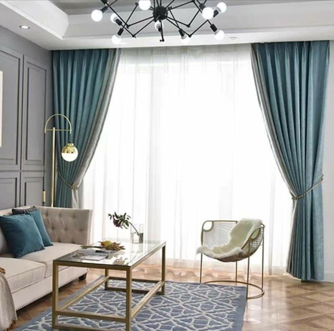 Elegante sala de estar con cortinas color turquesa, sofá capitoné, mesa de centro de cristal y alfombra azul estampada.