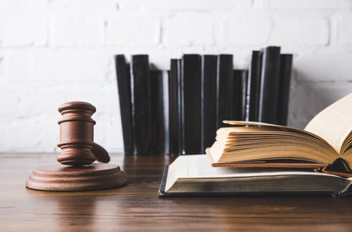 A wooden judge 's gavel is sitting on top of an open book on a wooden table.