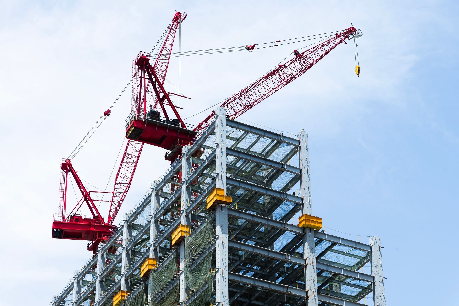 Red construction crane atop a steel-frame building under construction against a blue sky.