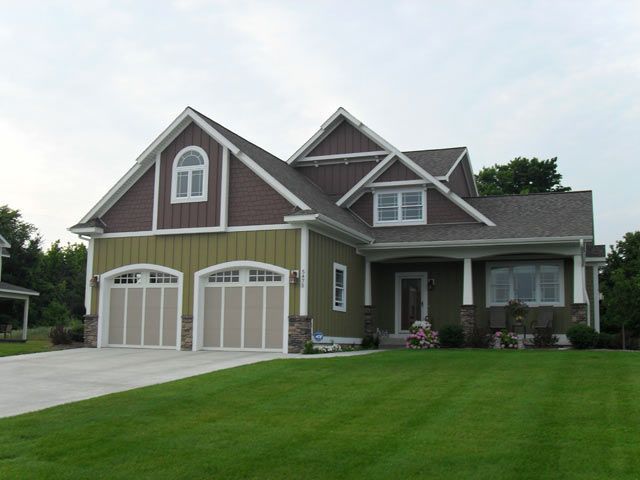 House with green siding, brown roof, two-car garage, and green lawn.