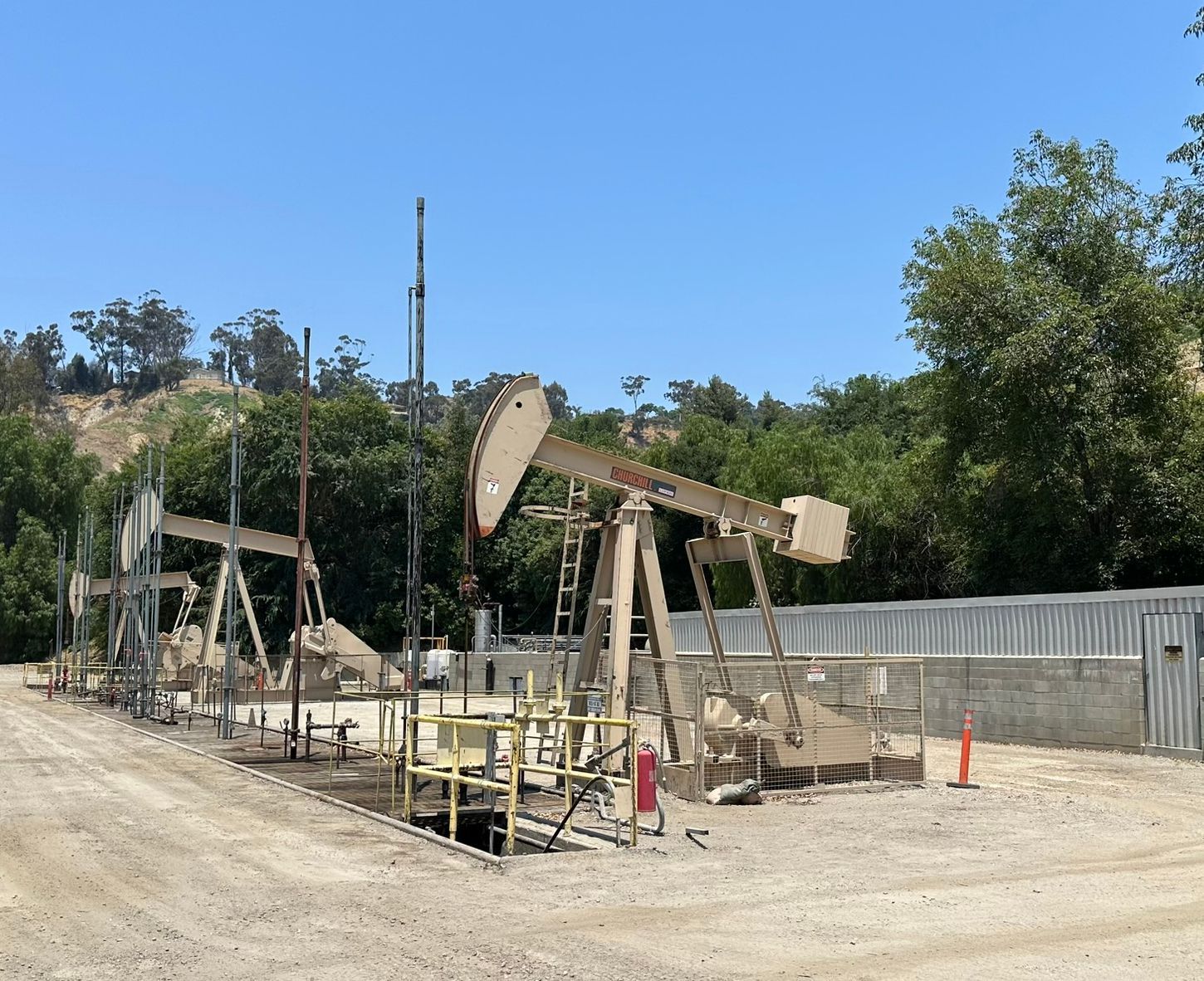 Oil pump jack operating in a dirt field beside a road under a clear blue sky
