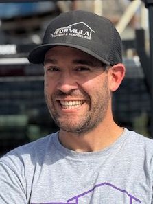 Man wearing a black hat with a logo smiles, possibly outdoors.