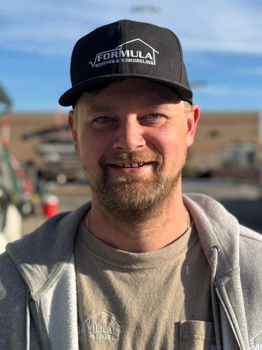 Man wearing a black hat with a logo smiles at the camera, outdoors.