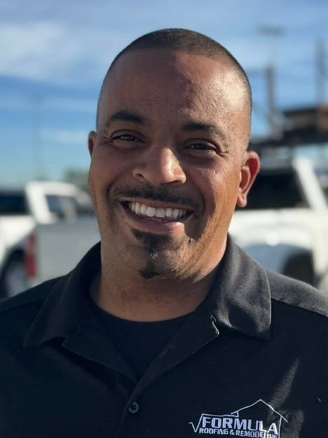 Man smiling, wearing a black shirt with business logo, set outdoors on a sunny day.