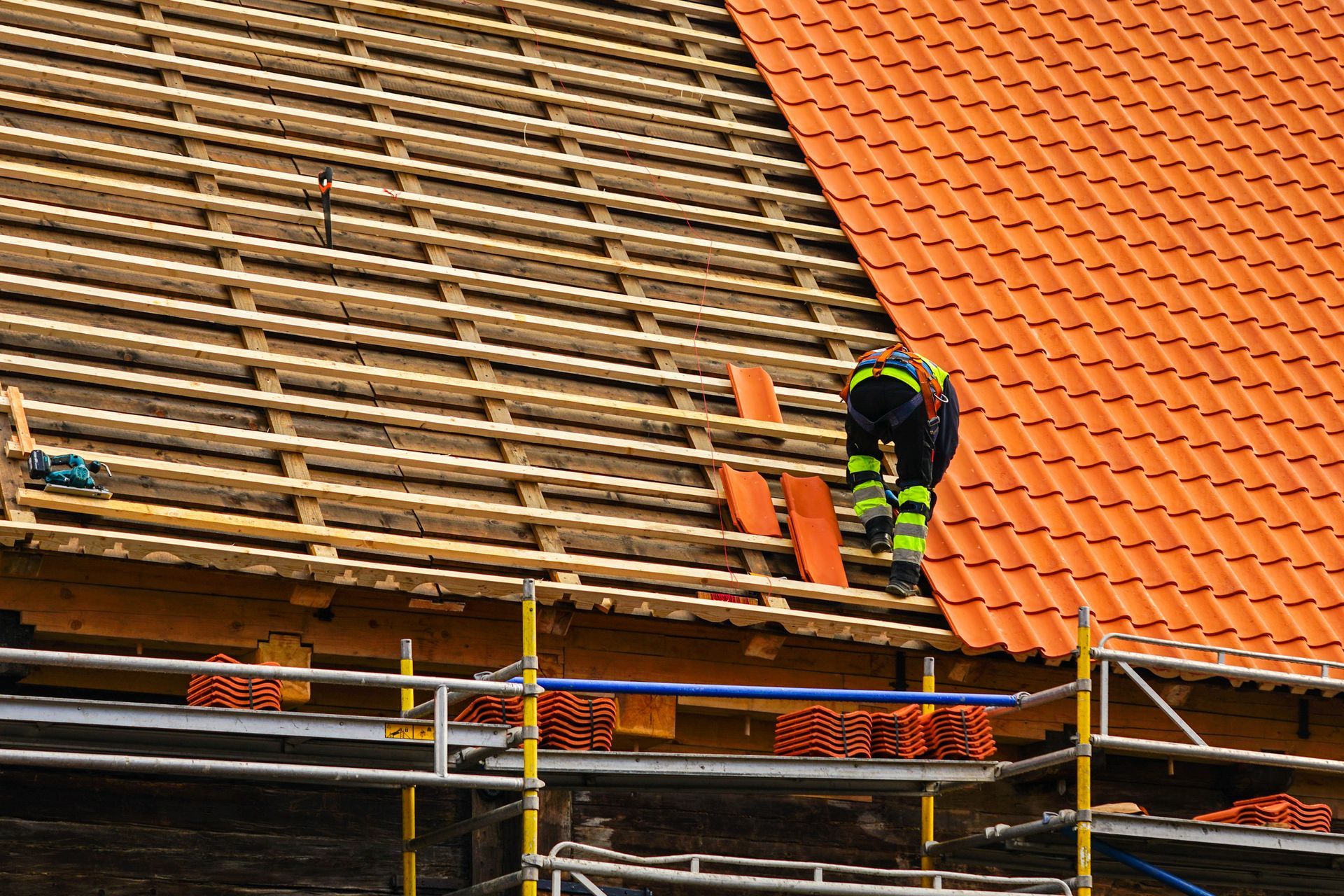 A male roofer in safety gear is installing new tiles during a roof replacement project.