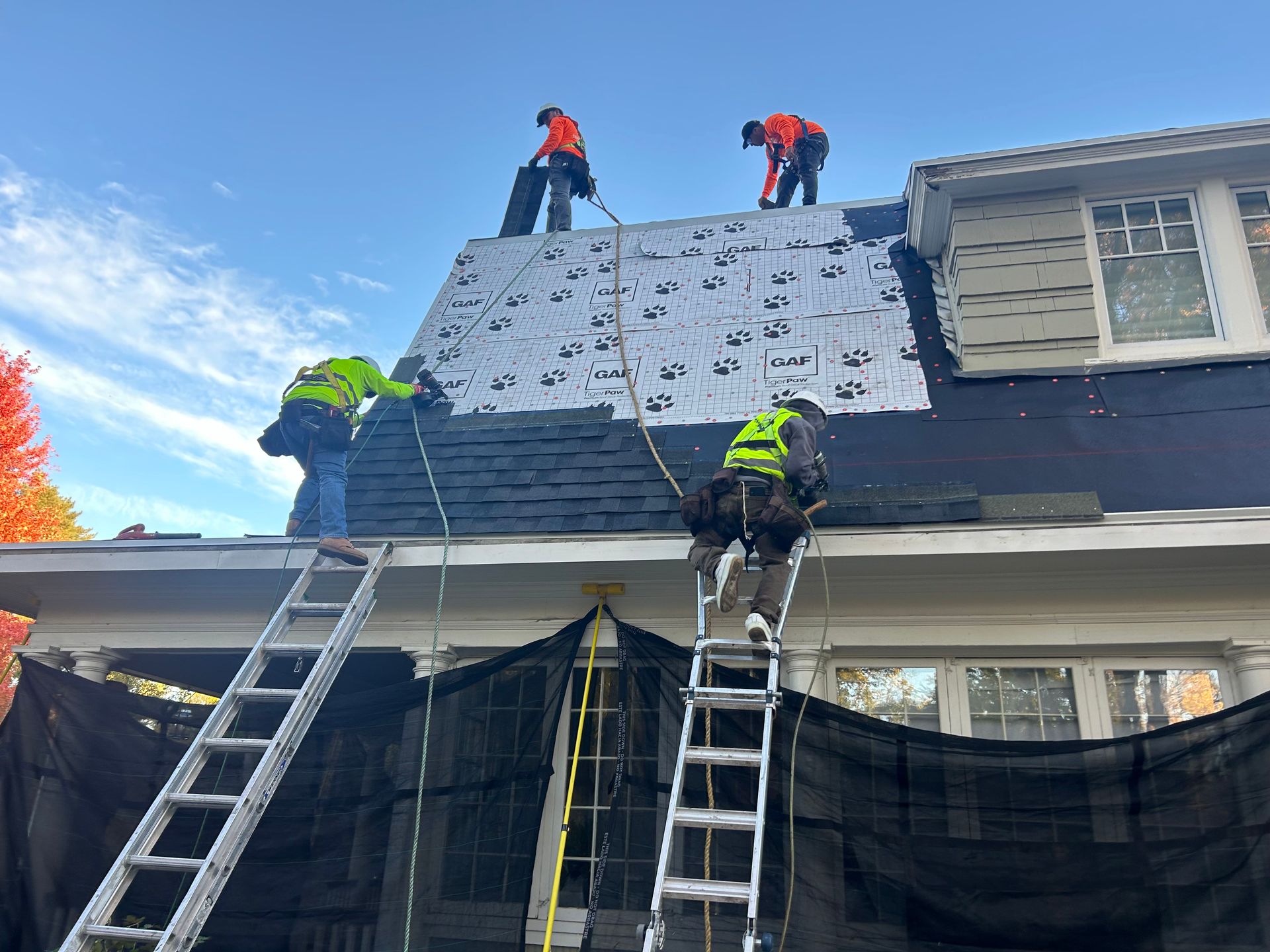Four men performing roof repairs on a house, using tools and safety gear for maintenance work. Four men performing roof repairs on a house, using tools and safety gear for maintenance work.