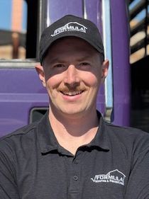 Man in black cap and polo, smiling, in front of a purple truck.