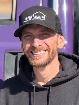 Man in black cap and hoodie smiling, with a semi-truck visible behind him.