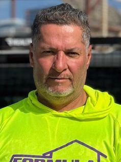 Man in a neon green hoodie, looking directly at the camera. Outdoor setting, logo visible.
