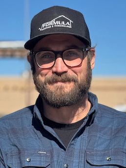 Man wearing glasses and a baseball cap smiling outdoors.