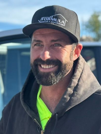 Man in black cap with beard smiles, wearing a hoodie and neon shirt, outdoors.