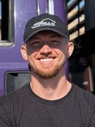 Man with a beard and baseball cap smiles in front of a purple truck.