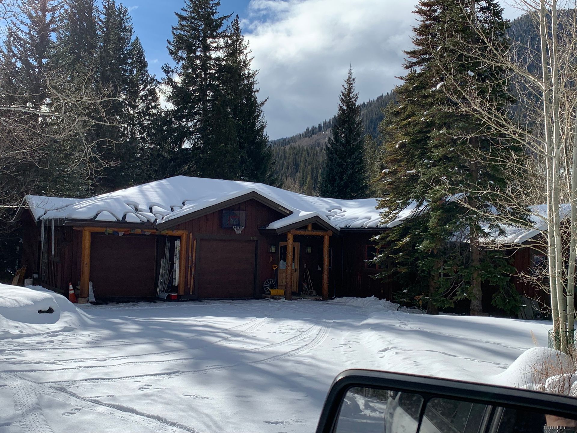 Snow-covered cabin in a wooded mountain area, with tall evergreens and a driveway in the foreground Snow-covered cabin in a wooded mountain area, with tall evergreens and a driveway in the foreground