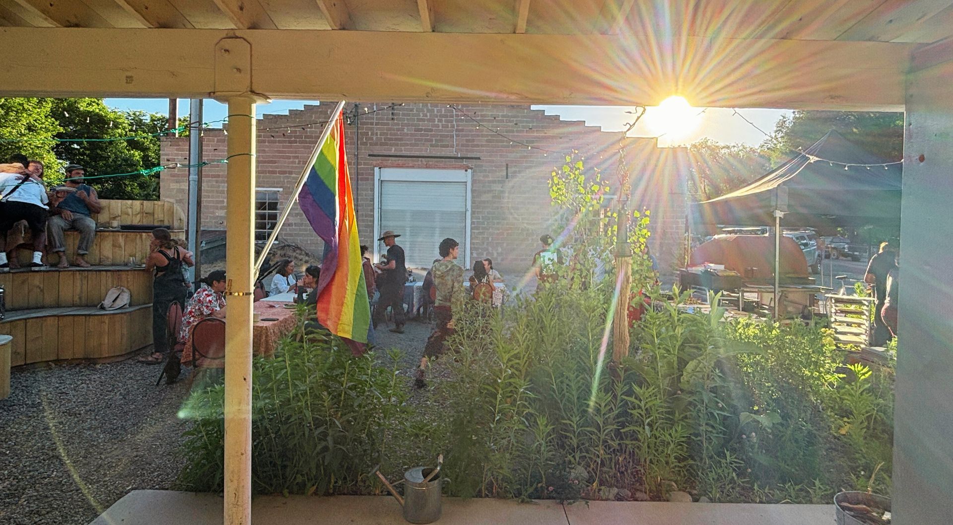 Backyard gathering at sunset with rainbow pride flag and people under a patio roof