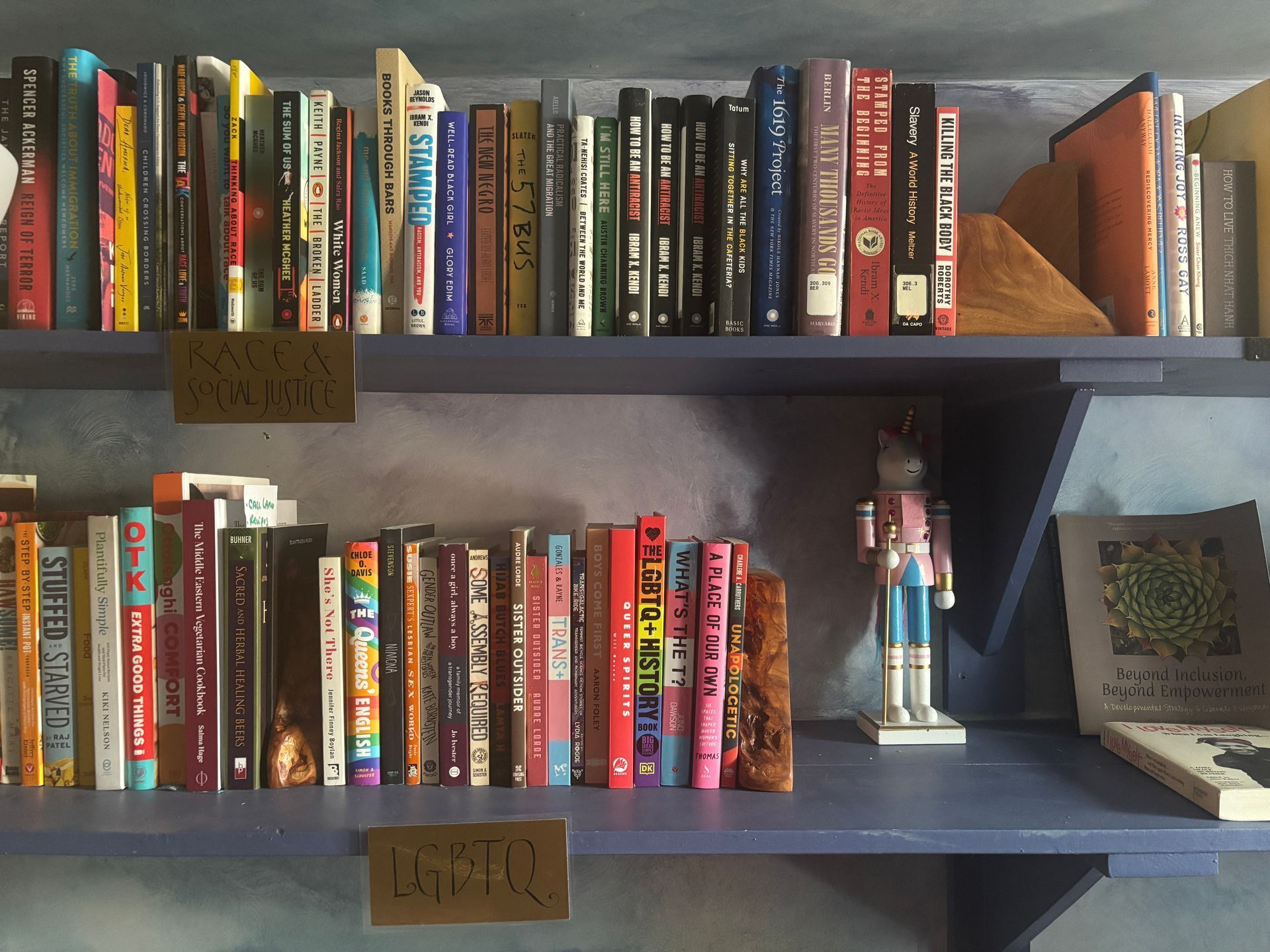 Two shelves of colorful books with small decor items in a home library.