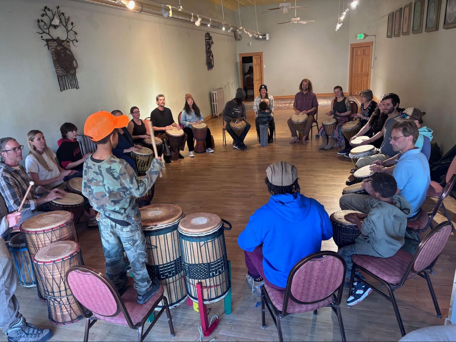 People seated in a circle playing hand drums in a bright studio room