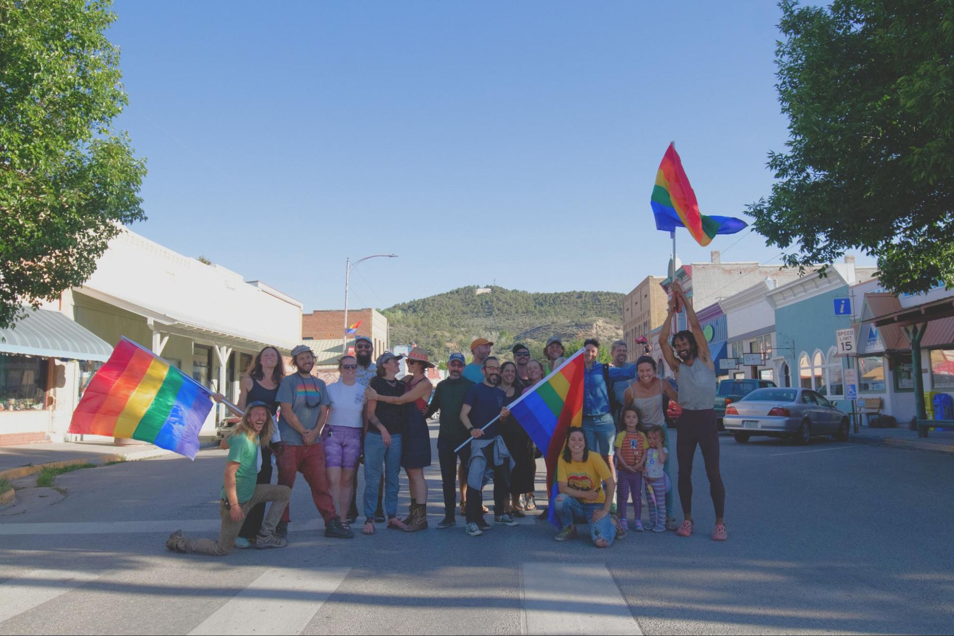 Group of people holding rainbow flags in a street parade under a clear blue sky