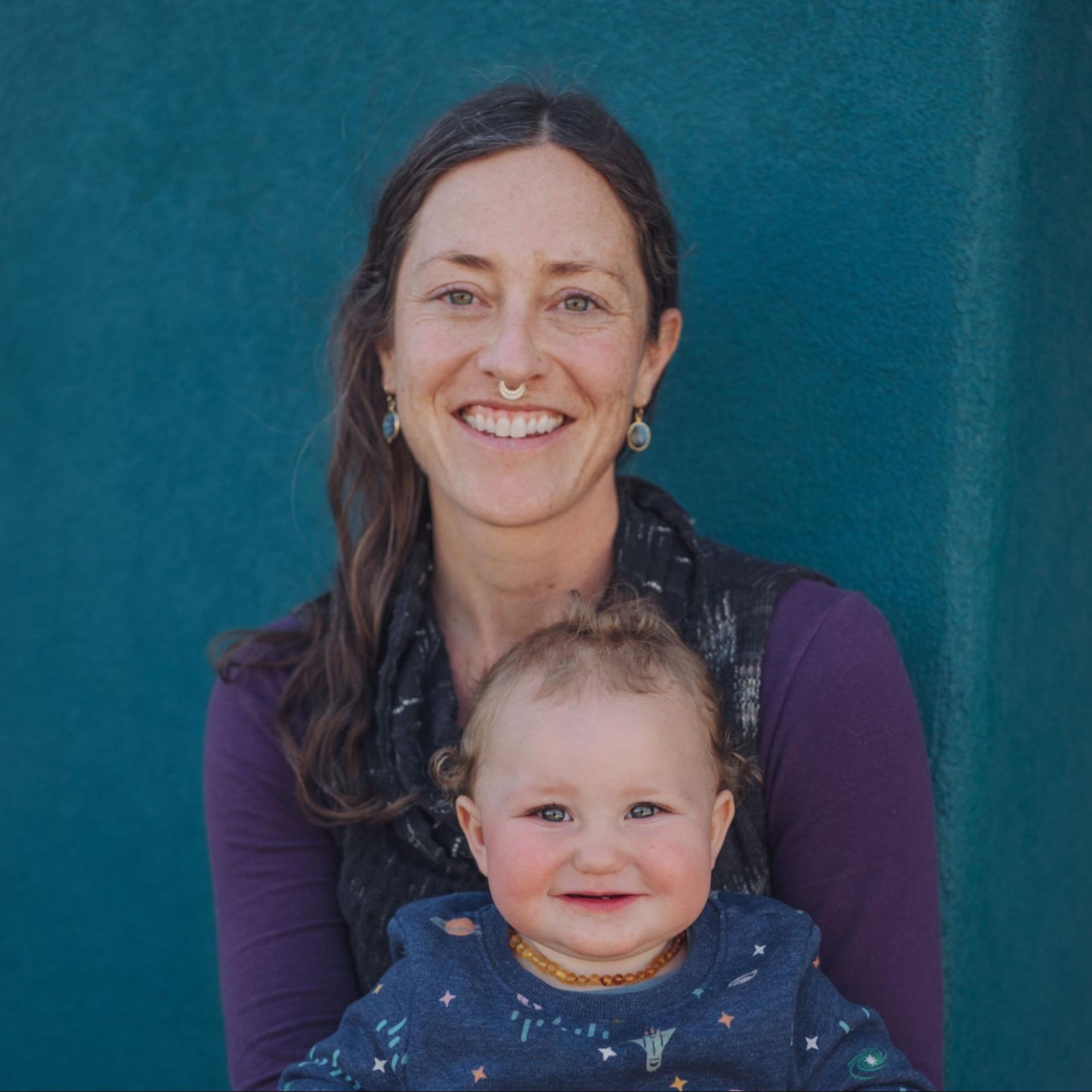 Smiling woman holding a smiling baby against a teal background