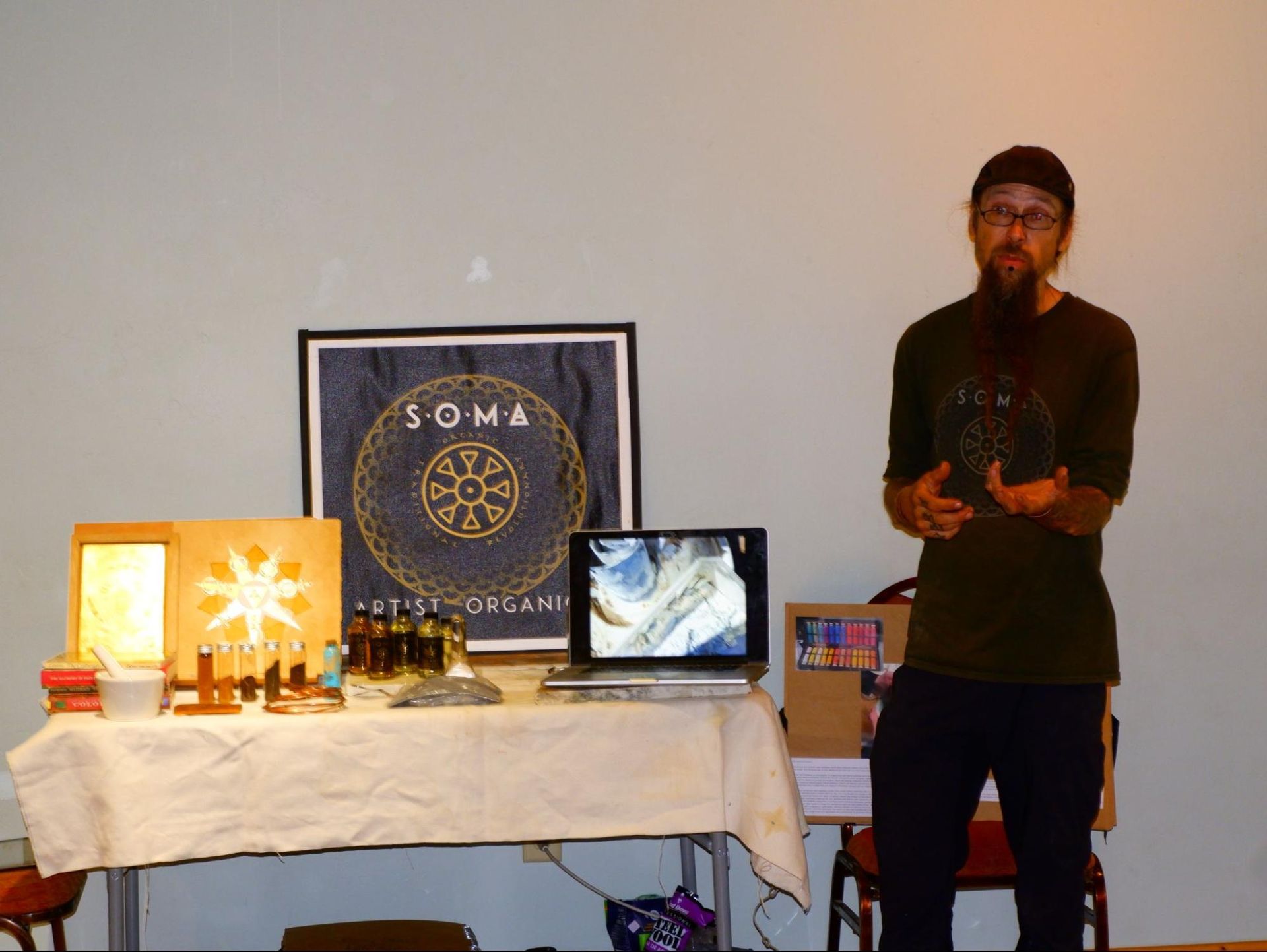Person standing beside a display table with lamps, a laptop, and a SOMA banner on the wall
