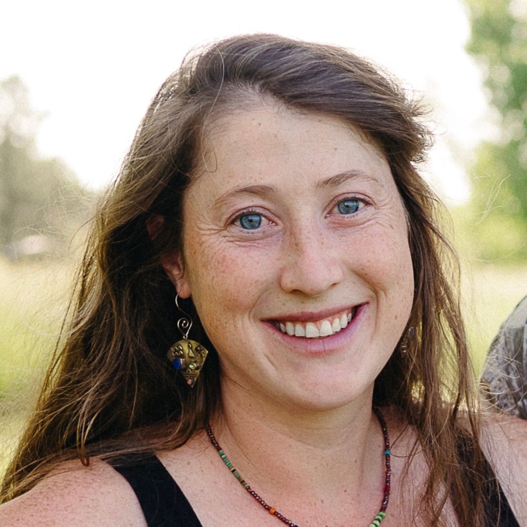 Smiling woman with long brown hair outdoors in a sunny field