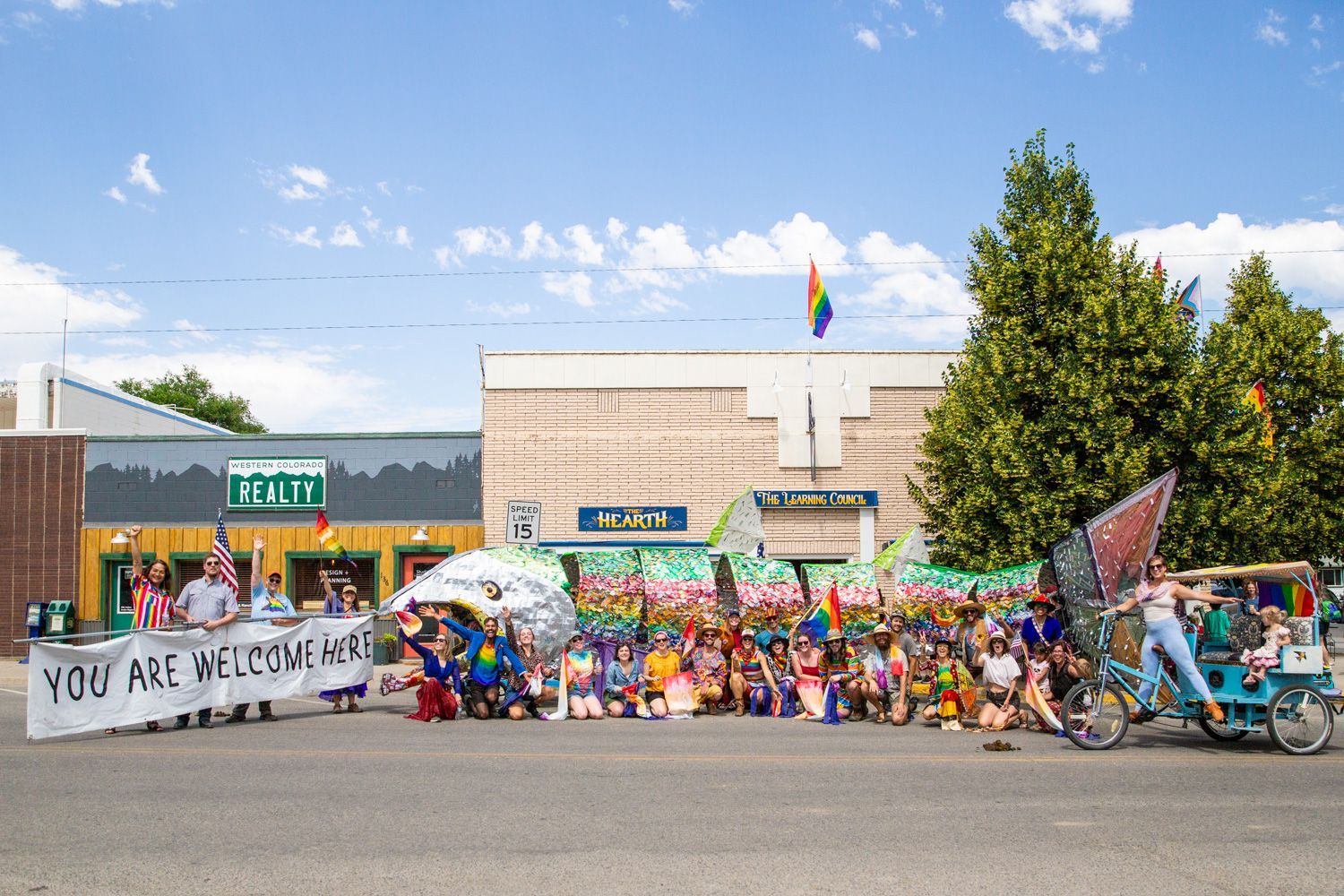 Colorful pride parade with banners and flags in front of a building on a sunny day