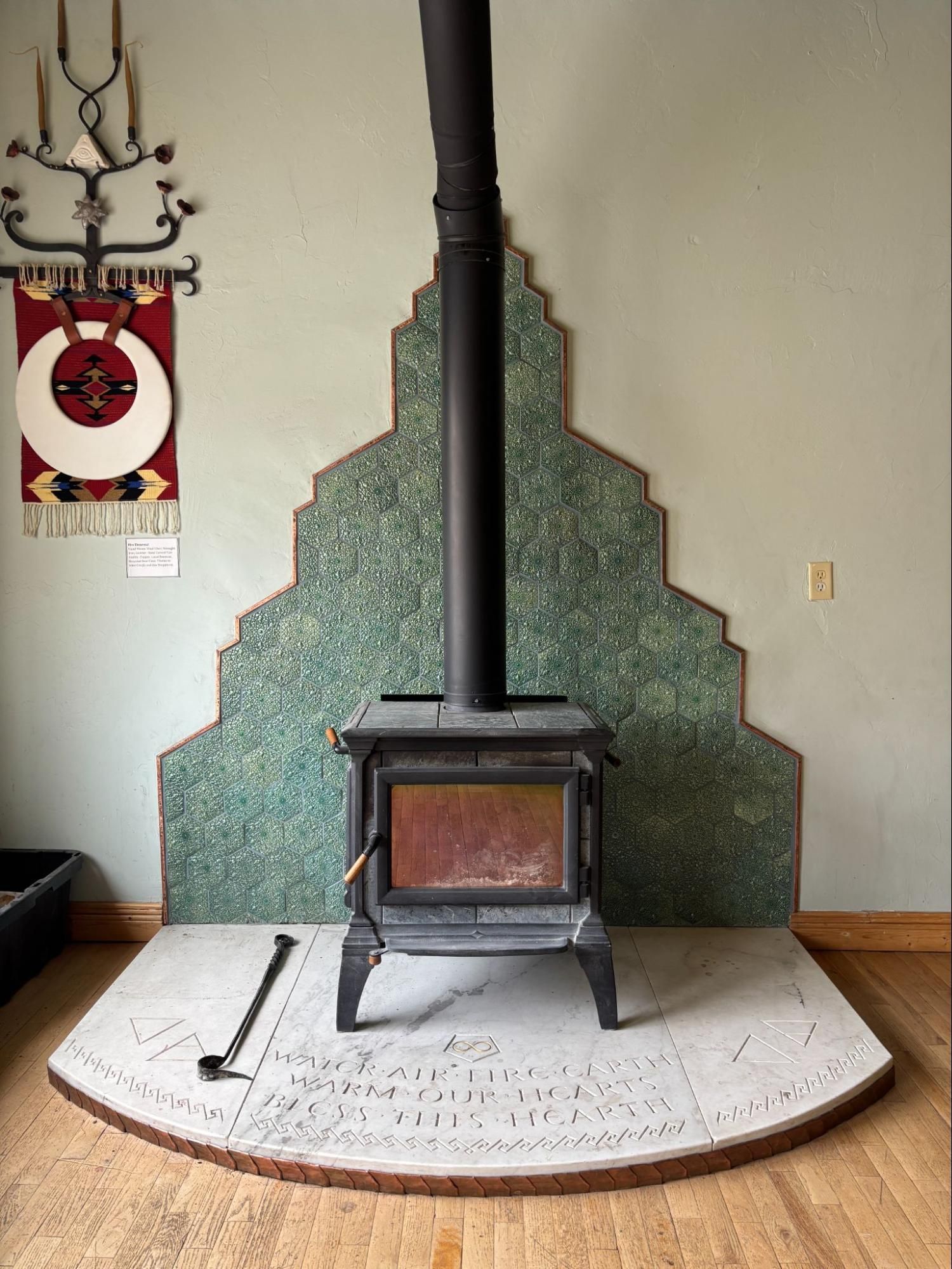 Wood stove centered on a white hearth in front of a green tiled wall panel