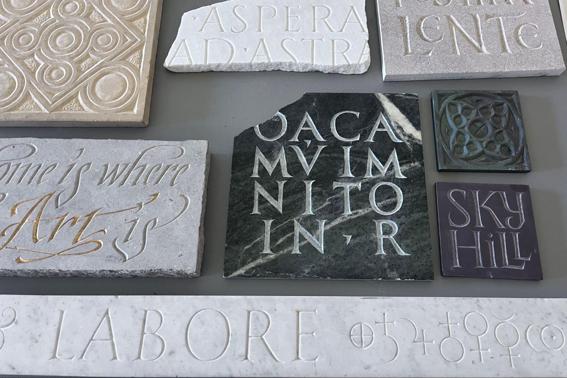 Assorted engraved stone and tile plaques with decorative Latin text in gray, white, and black.