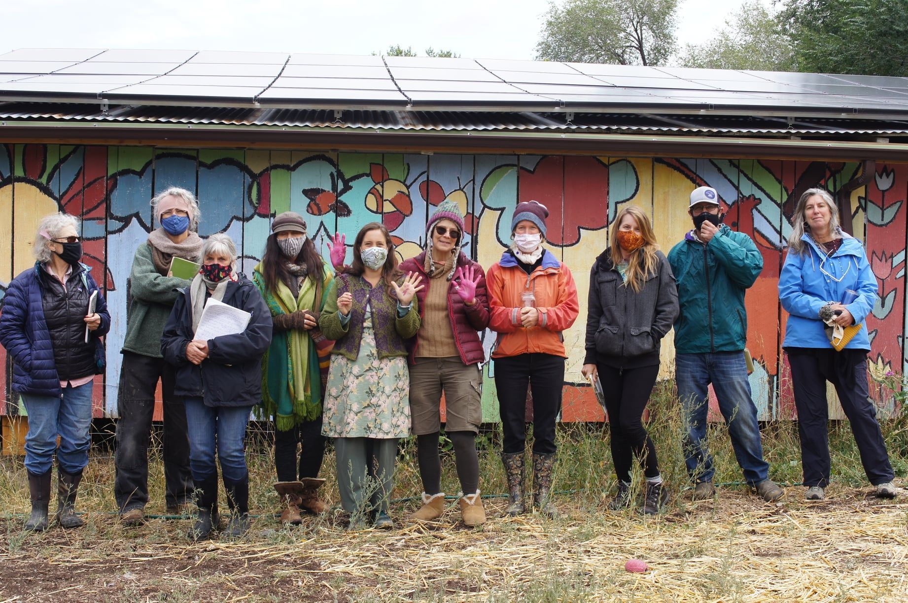 Group of people wearing masks standing outdoors in front of a colorful mural wall