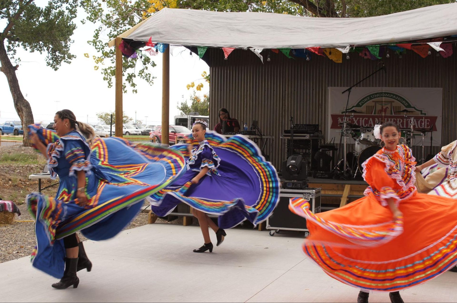 Dancers in bright blue and orange folkloric dresses performing outdoors on a stage