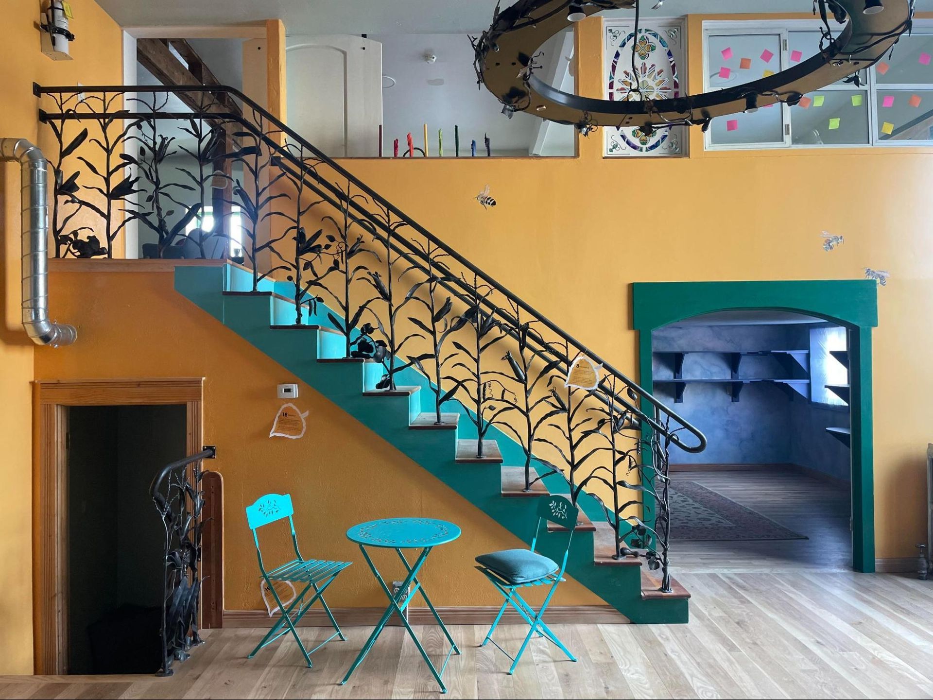 Colorful café interior with turquoise stairs, yellow walls, a small table, and a doorway to a back room