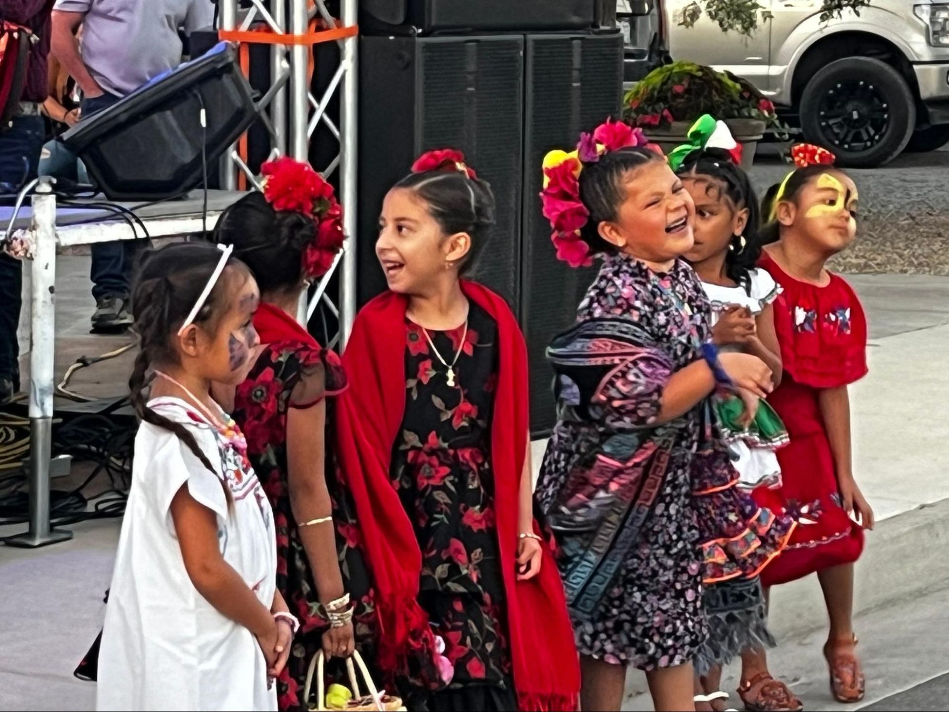 Children in colorful traditional outfits smiling and dancing outdoors at a cultural event