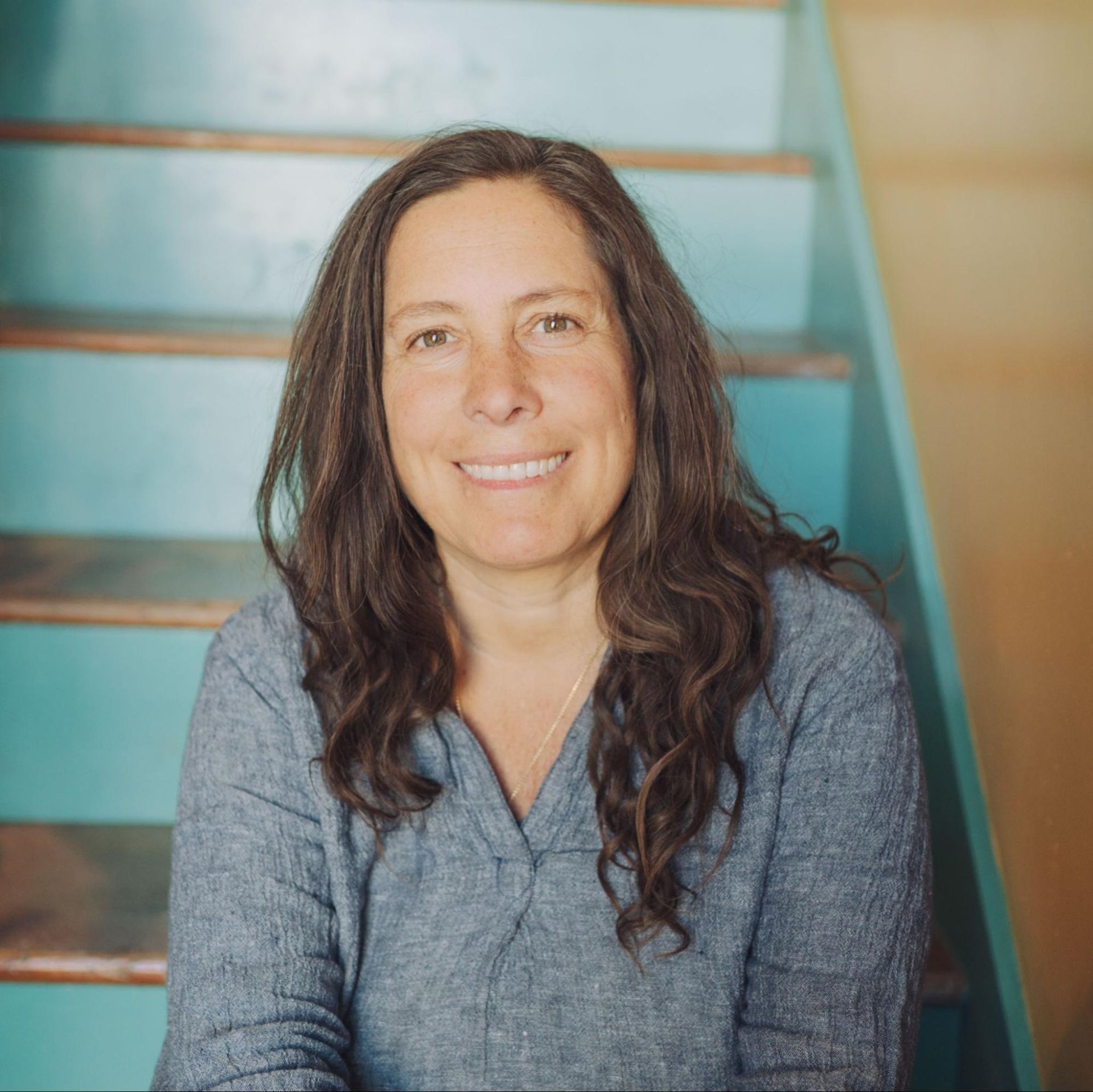 Woman smiling on teal staircase, wearing a gray sweater.