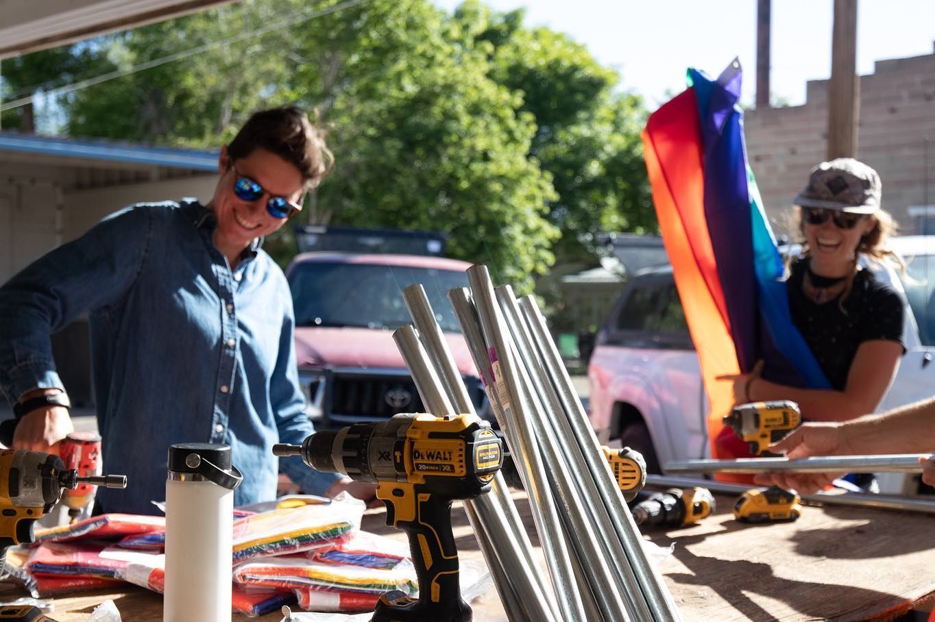 Two people working at a table outdoors with tools and colorful materials in bright sunlight